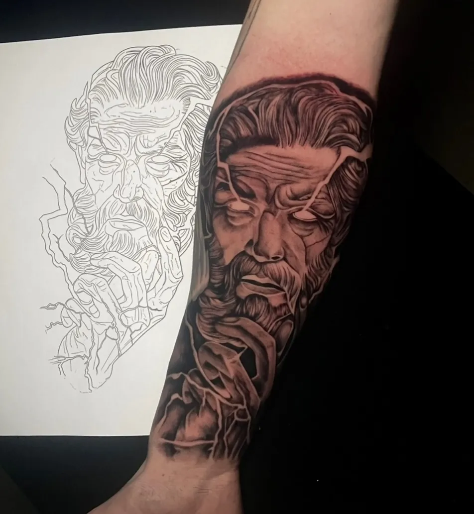 Fertiges Schwarzgrau-Tattoo am Arm neben der Bleistiftvorzeichnung auf Papier